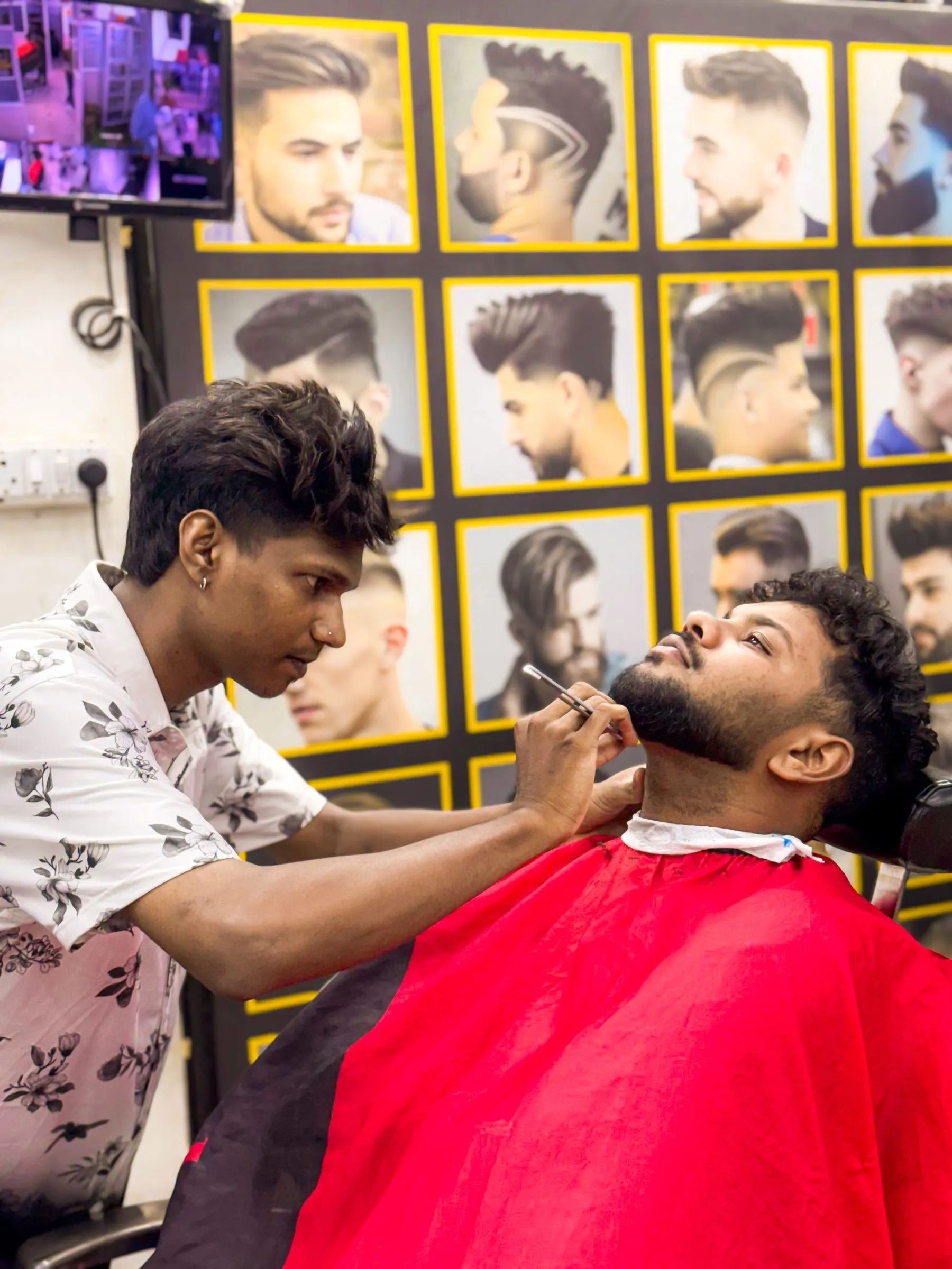 A barber detailing a customer’s beard line with a razor, the customer reclined in the chair