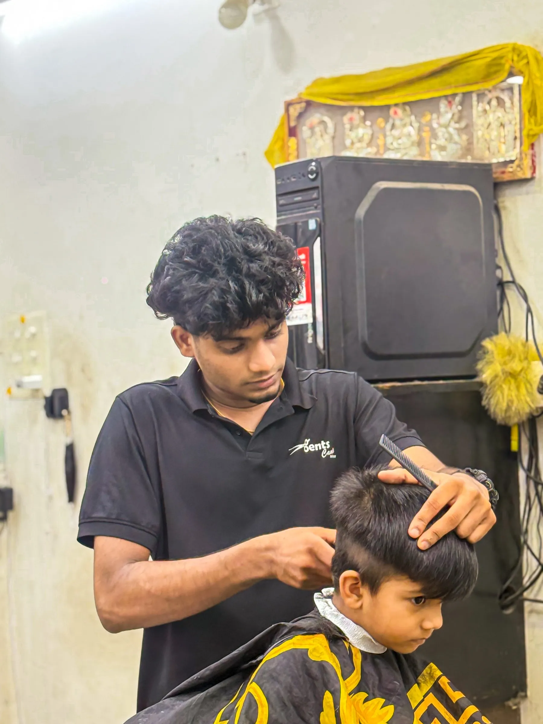 A Gents Camp barber in the shop polo cutting a young boy’s hair